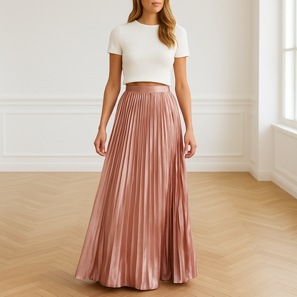 Vrouw draagt een elegante, geplooide maxi-rok in satijnachtige licht roze blushkleur met glanzende afwerking – high waist en vloeiende pasvorm, perfect voor lente en zomer.